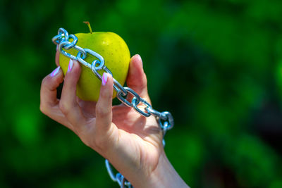 Cropped hand of woman holding granny smith apple with chain