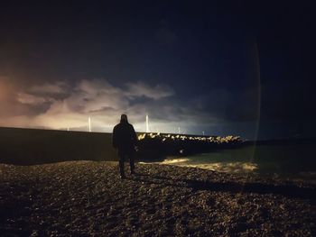 Rear view of silhouette man standing on illuminated street against sky