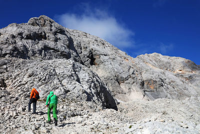 Rear view of men standing by rocky mountains against sky