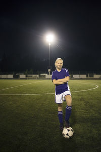 Portrait of girl standing with arms crossed on soccer field against sky at night