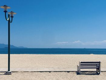 Bench on beach against blue sky