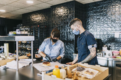 Male coworker standing by female chef preparing meal at kitchen counter in restaurant