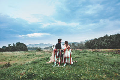 Rear view of wedding couple sitting on chairs at farm