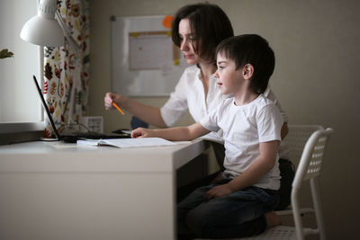 Tutor deals with the preschooler with a laptop, a real home interior, the concept of childhood 