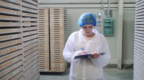 Woman writing on document while working in factory