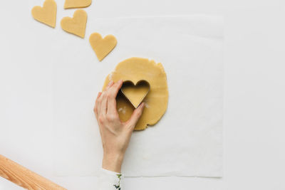 Cropped hand of woman using heart shape cutter on dough