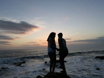 Silhouette friends standing on beach against sky during sunset