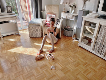 Full length of woman sitting on wooden floor at home