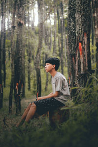 Side view of young man sitting on tree trunk in forest