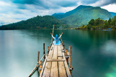 Woman sitting on pier over lake