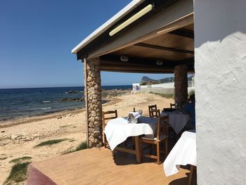 Chairs and table on beach against clear sky