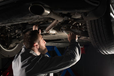 Side view of mechanic repairing car at garage