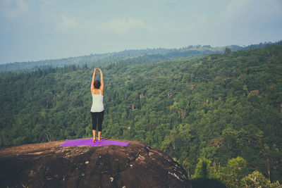 Rear view of woman exercising on cliff
