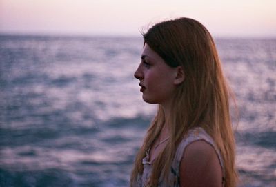 Profile view of young woman standing against sea during sunset
