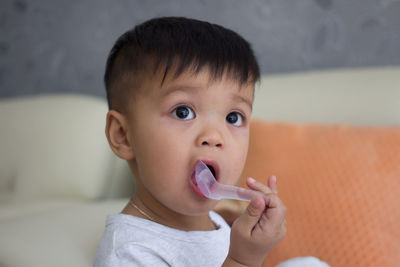 Cute baby boy biting spoon while looking away at home
