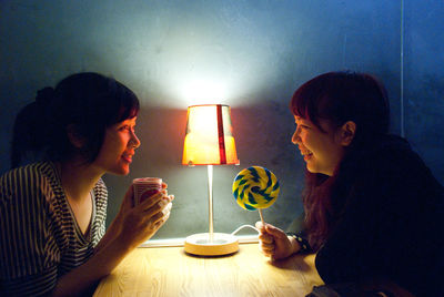 Women talking while holding coffee cup and lollipop sitting by table at home