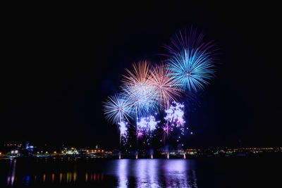 Firework display in city against sky at night