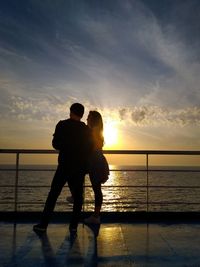 Couple standing on boat deck against sky during sunset