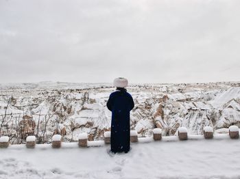 Rear view of man in traditional clothing standing on snowy field against sky