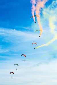 Low angle view of people paragliding against sky