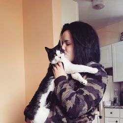 Young woman kissing cat while standing at home
