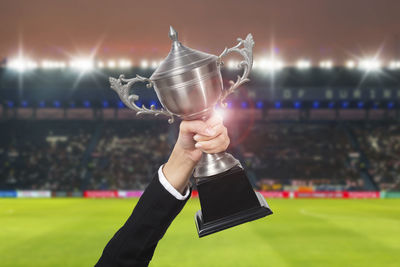 Cropped hand of businesswoman holding trophy at stadium