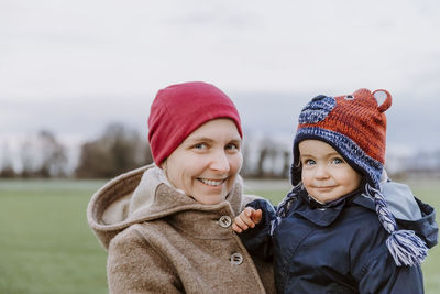 Portrait of smiling mother holding girl on field during winter