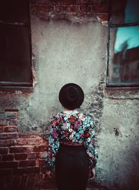 Rear view of woman standing against old wall