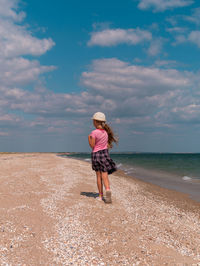Happy child in straw hat running jumping having fun on empty autumn beach blond girl walking on sand
