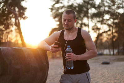 Man listening music from smart phone while holding water bottle by tire