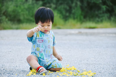 Full length of cute boy playing while siting on road