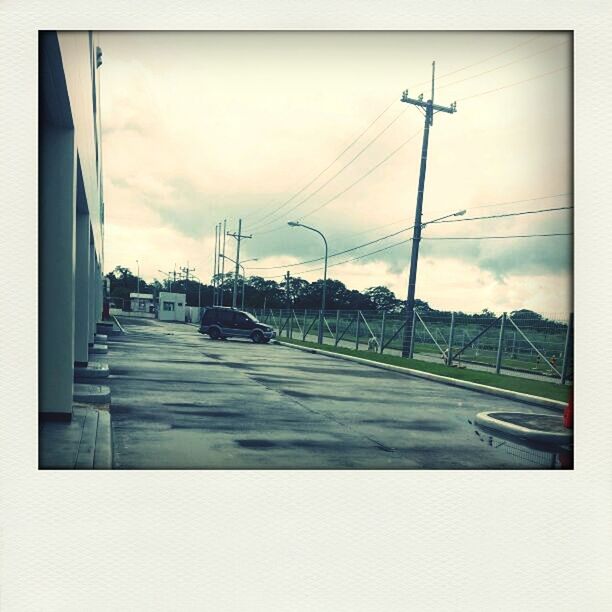 transfer print, transportation, sky, car, auto post production filter, road, street light, land vehicle, mode of transport, cloud - sky, street, the way forward, cloudy, cloud, electricity pylon, empty, built structure, power line, diminishing perspective, road marking