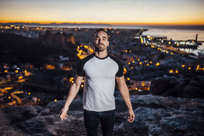 Full length of young man standing against cityscape during sunset