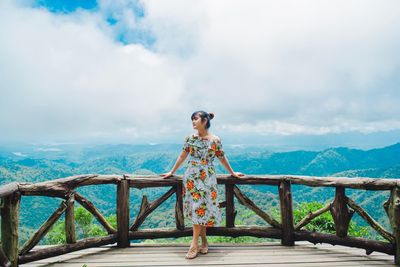 Woman standing on railing by mountain against sky