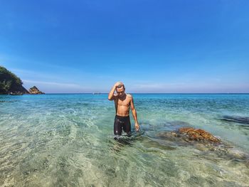 Shirtless man standing on seashore against sky