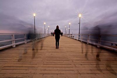 Rear view of man walking on illuminated bridge against sky