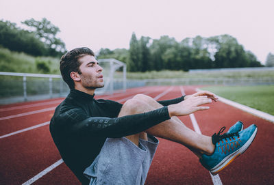 Side view of young man sitting on running track