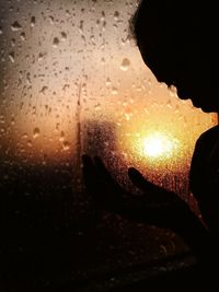 Close-up of wet glass window against sky during sunset