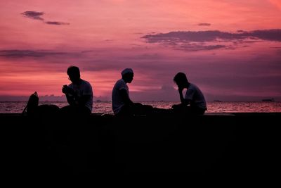 Silhouette people sitting on beach during sunset