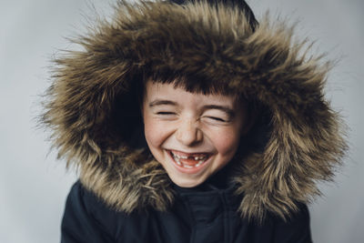 Close-up of happy boy in fur coat standing against white background