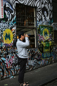 Full length of man photographing with graffiti on wall