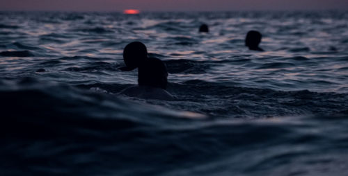 Silhouette people swimming in sea during sunset