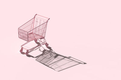 Close-up of shopping cart against pink background