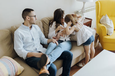 Older sister holding her newborn baby brother next to their parents on the sofa