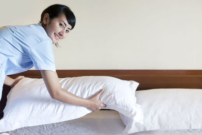 Portrait of smiling woman adjusting pillow on bed