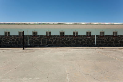 Empty road by buildings against clear blue sky