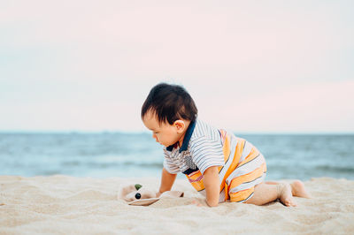 Boy playing on sand at beach against sky