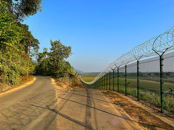 Road amidst trees against clear blue sky