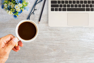 Directly above shot of hand holding coffee cup on table