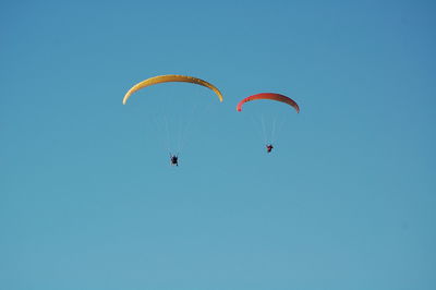 Low angle view of people paragliding against clear sky